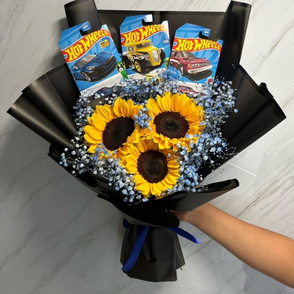 Ramo de tres girasoles con gypsophila azul y carritos Hot Wheels en papel negro — Wallflower Guatemala